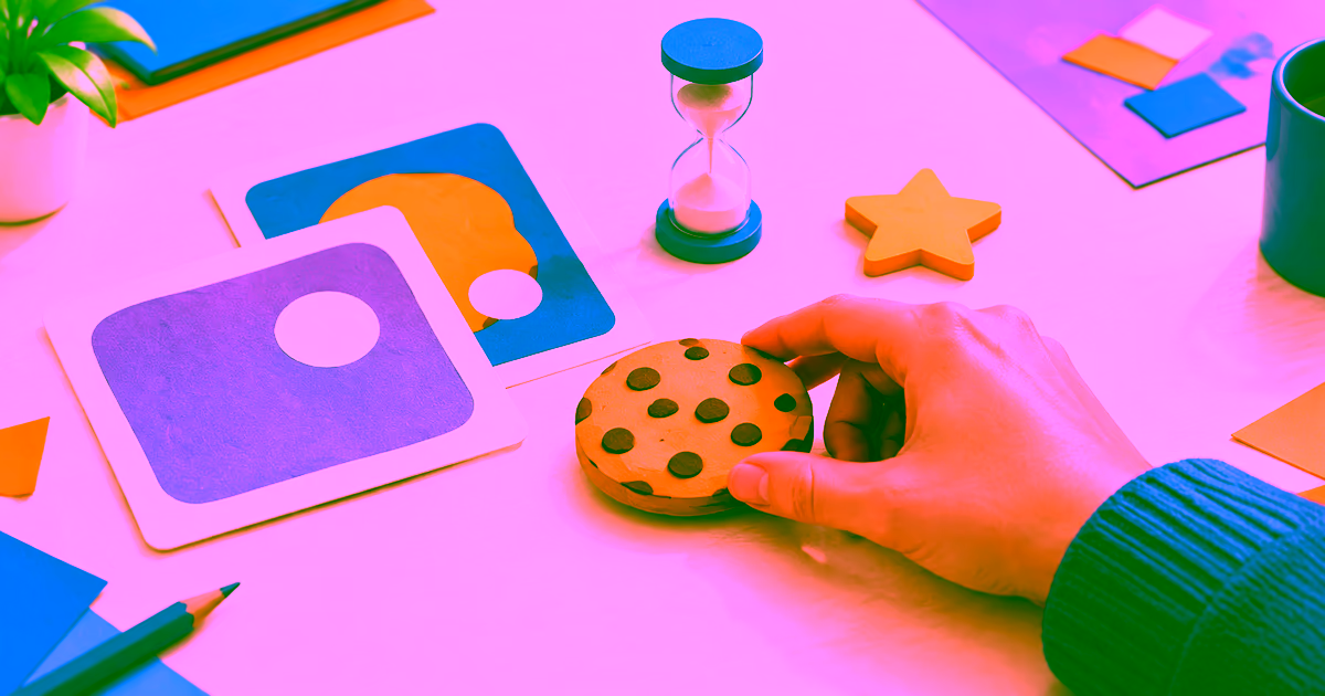 A hand tests a cookie game token beside rough layout cards, an hourglass, and a score star